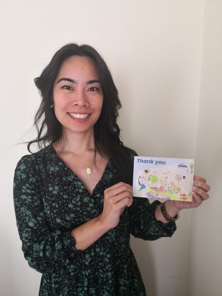 young woman with dark hair wearing a dress and smiling holding a thank you card from a mentee 