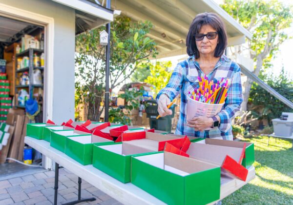 A woman places items into green Christmas boxes 